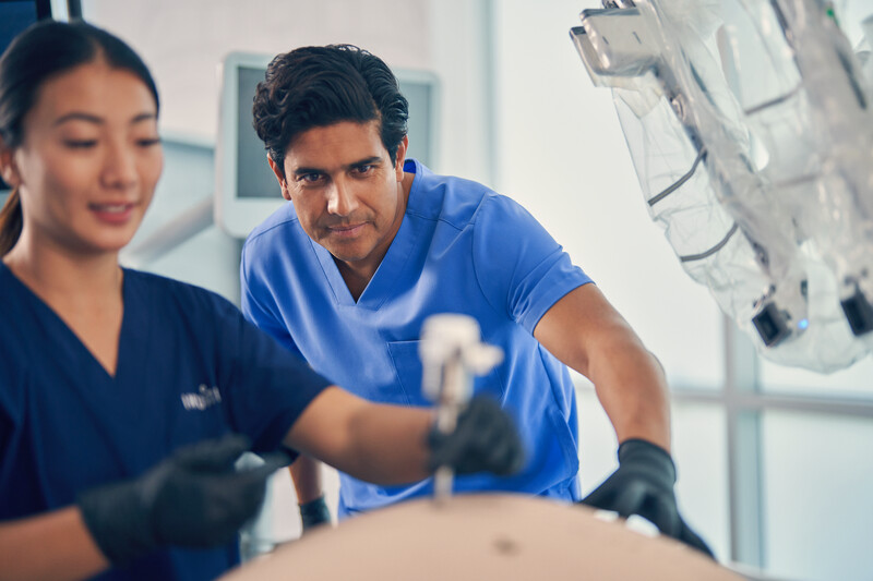 Surgeon watching over employee practicing procedure on test equipment
